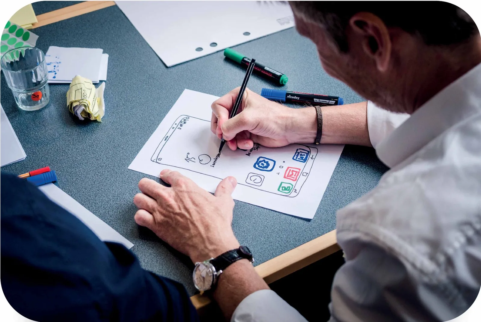 A designer sketches a mobile app screen with pens on paper